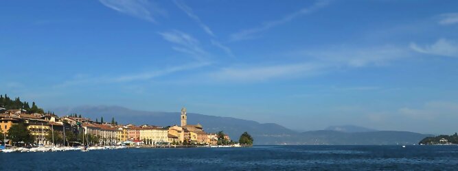Trip Vorarlberg beliebte Urlaubsziele am Gardasee -  Mit einer Fläche von 370 km² ist der Gardasee der größte See Italiens. Es liegt am Fuße der Alpen und erstreckt sich über drei Staaten: Lombardei, Venetien und Trentino. Die maximale Tiefe des Sees beträgt 346 m, er hat eine längliche Form und sein nördliches Ende ist sehr schmal. Dort ist der See von den Bergen der Gruppo di Baldo umgeben. Du trittst aus deinem gemütlichen Hotelzimmer und es begrüßt dich die warme italienische Sonne. Du blickst auf den atemberaubenden Gardasee, der in zahlreichen Blautönen schimmert - von tiefem Dunkelblau bis zu funkelndem Türkis. Majestätische Berge umgeben dich, während die Brise sanft deine Haut streichelt und der Duft von blühenden Zitronenbäumen deine Nase kitzelt. Du schlenderst die malerischen, engen Gassen entlang, vorbei an farbenfrohen, blumengeschmückten Häusern. Vereinzelt unterbricht das fröhliche Lachen der Einheimischen die friedvolle Stille. Du fühlst dich wie in einem Traum, der nicht enden will. Jeder Schritt führt dich zu neuen Entdeckungen und Abenteuern. Du probierst die köstliche italienische Küche mit ihren frischen Zutaten und verführerischen Aromen. Die Sonne geht langsam unter und taucht den Himmel in ein leuchtendes Orange-rot - ein spektakulärer Anblick.